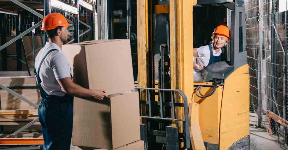 Dois funcionários em um armazém, com uma empilhadeira parada, representam a inatividade da empilhadeira.