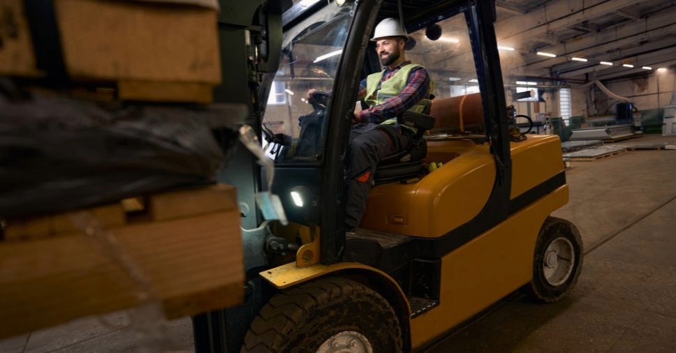 Operador qualificado manuseia carga pesada em ambiente industrial durante o uso de empilhadeira.