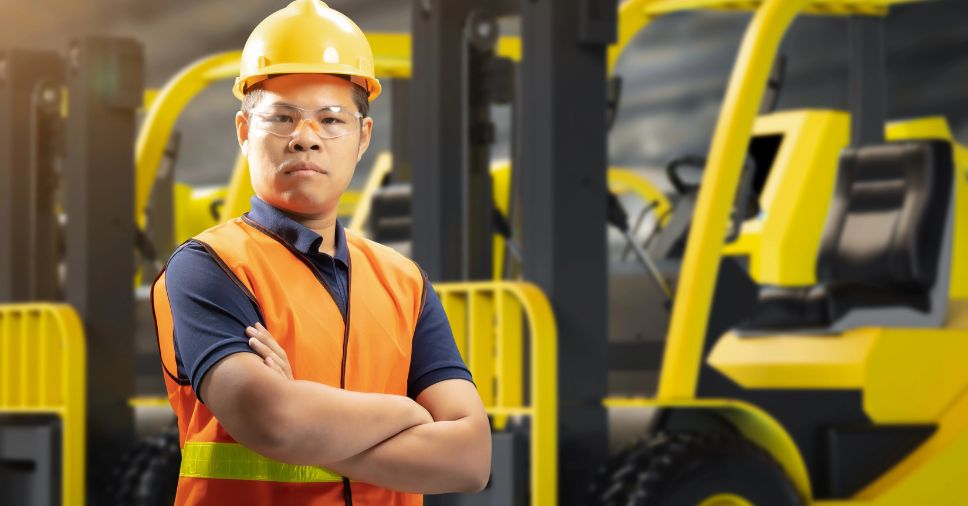 Trabalhador equipado com EPIs foca em evitar acidentes com empilhadeiras.
