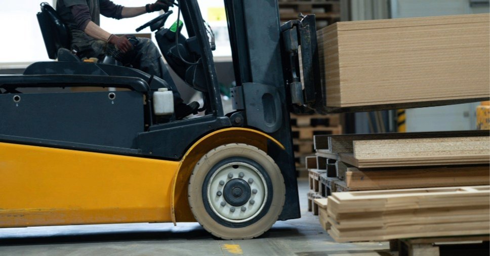 Veículo industrial amarelo erguendo placas de madeira em impacto no desempenho da empilhadeira.
