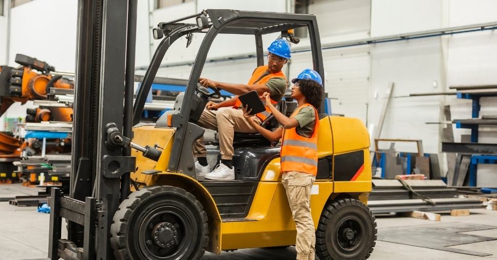 Trabalhadores com colete e prancheta analisam dados sobre aluguel de empilhadeiras para industria.