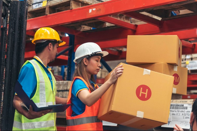Operadores de capacete organizam caixas de papelão para movimentação de cargas internas.